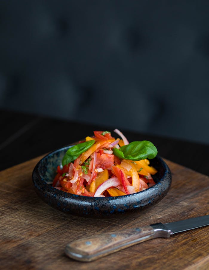 Fresh vegetable salad with colorful peppers and onions in a black bowl on a wooden board.